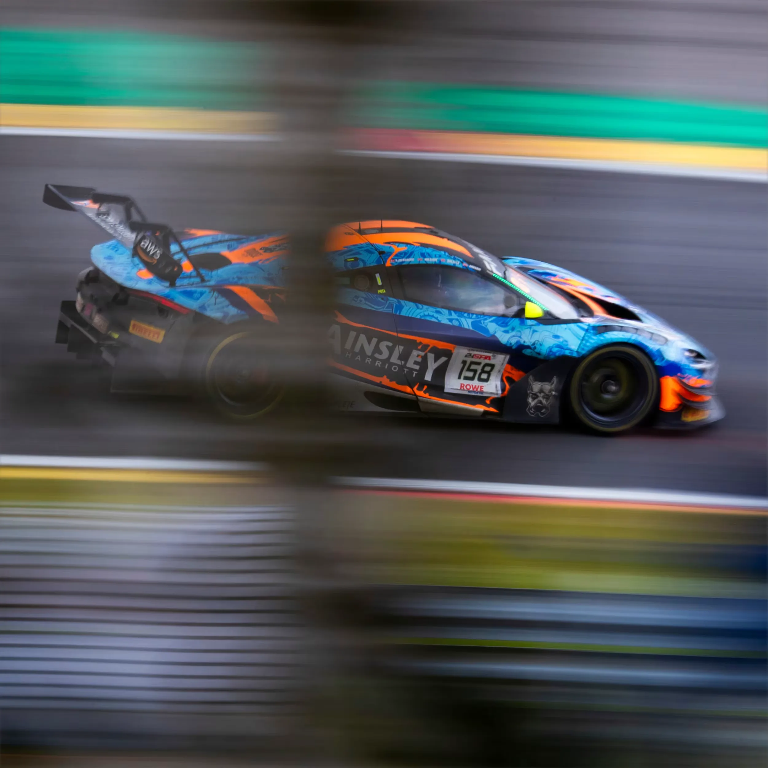 Two GT3 race cars in a motion-blurred panning shot, a blue-and-orange McLaren leading